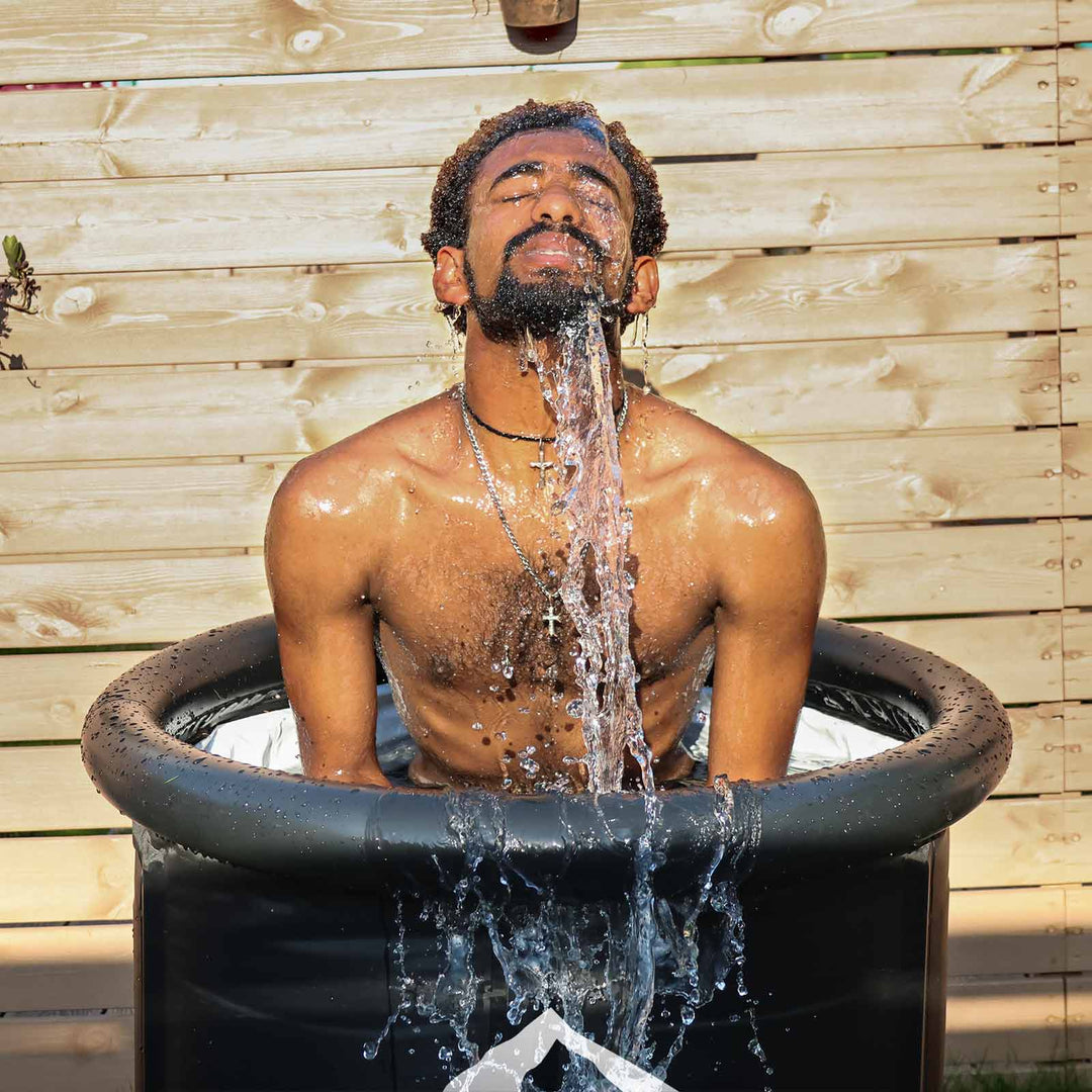 Man eyes closed in matte black portable cold plunge tub, water intensely splashing for an invigorating cold therapy.