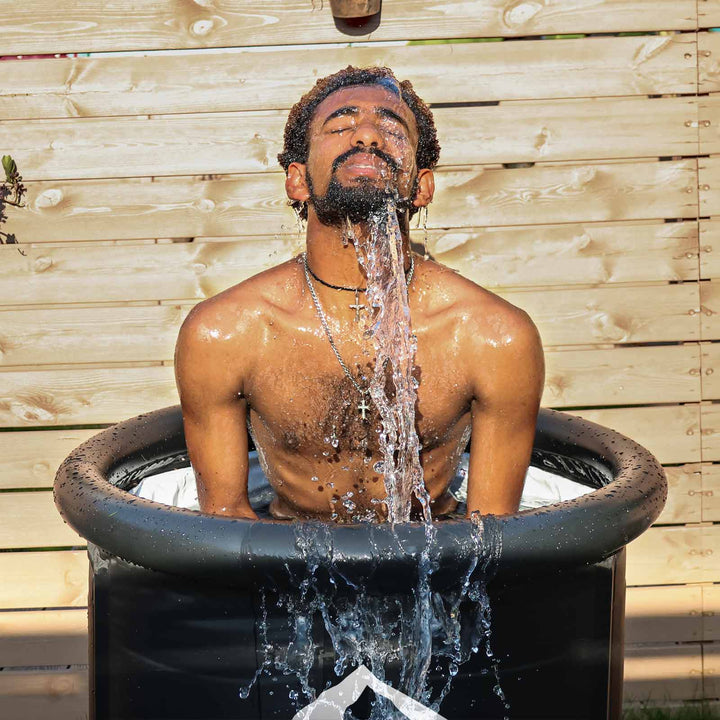 Man eyes closed in matte black portable cold plunge tub, water intensely splashing for an invigorating cold therapy.