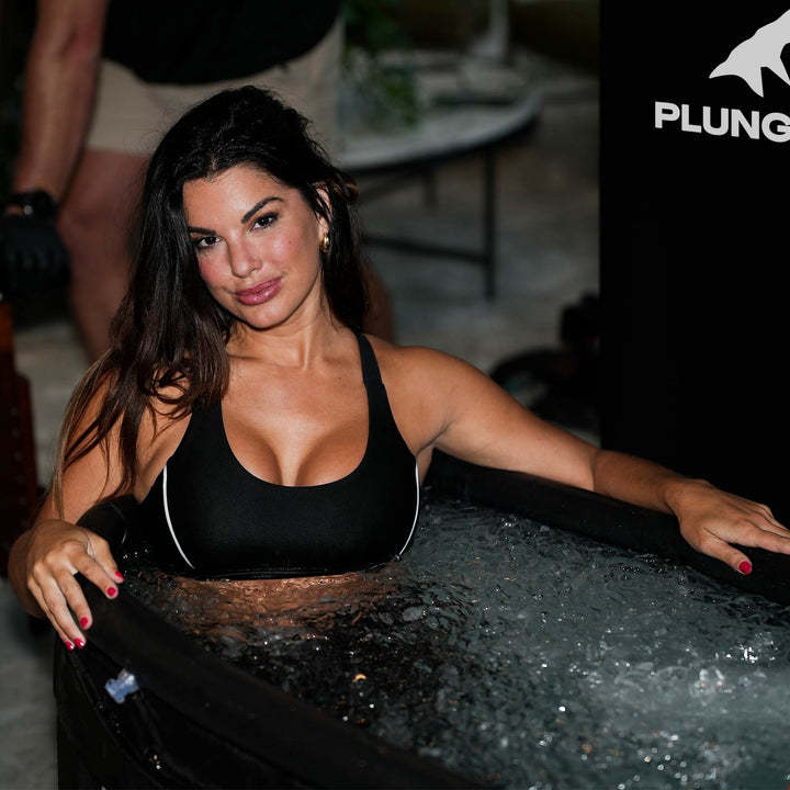 Woman smiling in a PLUNGE CHILL tub with icy water, wearing a sports bra.