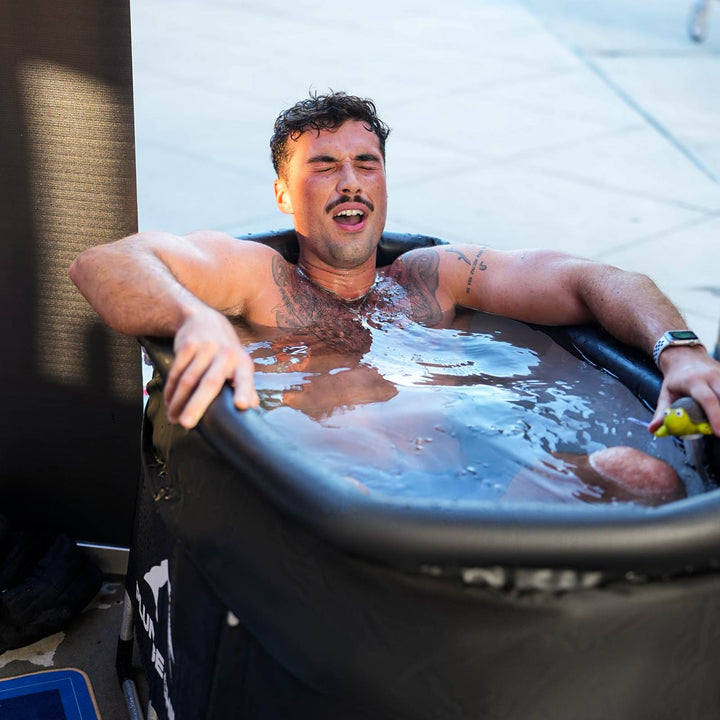 Man with tattoos immersed in a PLUNGE CHILL tub, eyes closed in reaction to the cold.