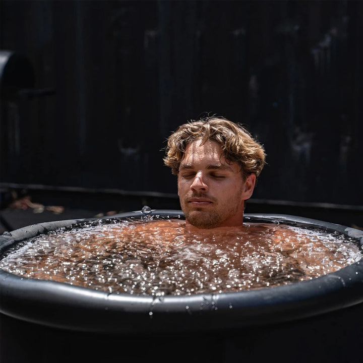 Relaxing man in a matte black portable cold plunge tub with icy, bubbling water. Ideal for home ice baths.