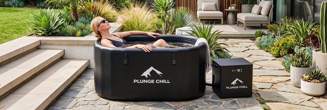 A woman wearing sunglasses is lying in an ice bath tub in her yard