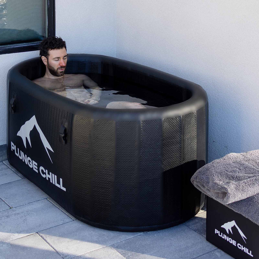 Man relaxing in a Plunge Chill inflatable black cold plunge tub with ice bath chiller system for recovery.