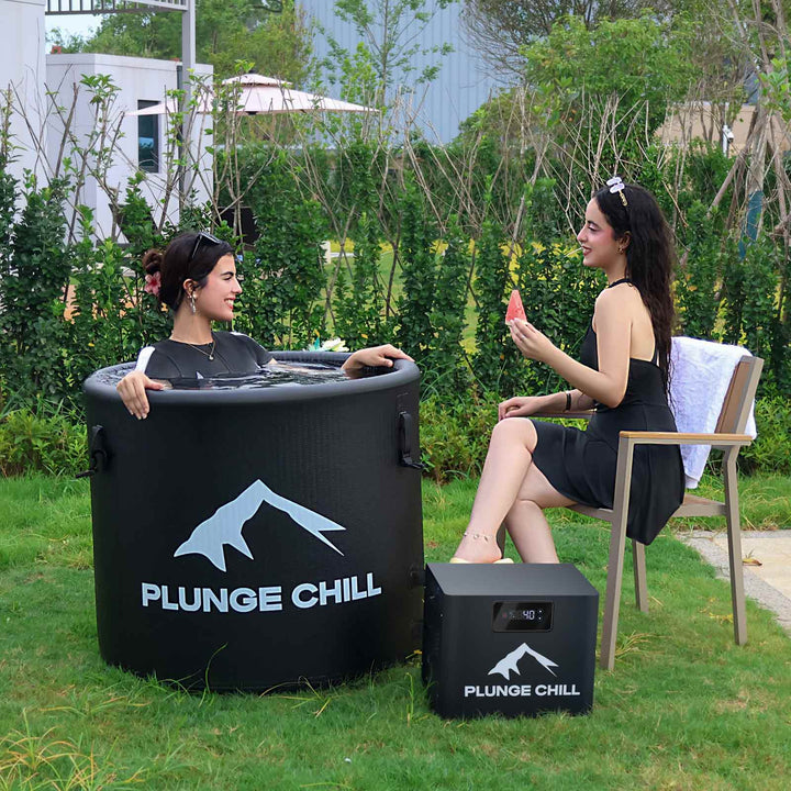 Two friends laughing together while sharing a Plunge Chill PVC cold plunge tub during an outdoor soak.