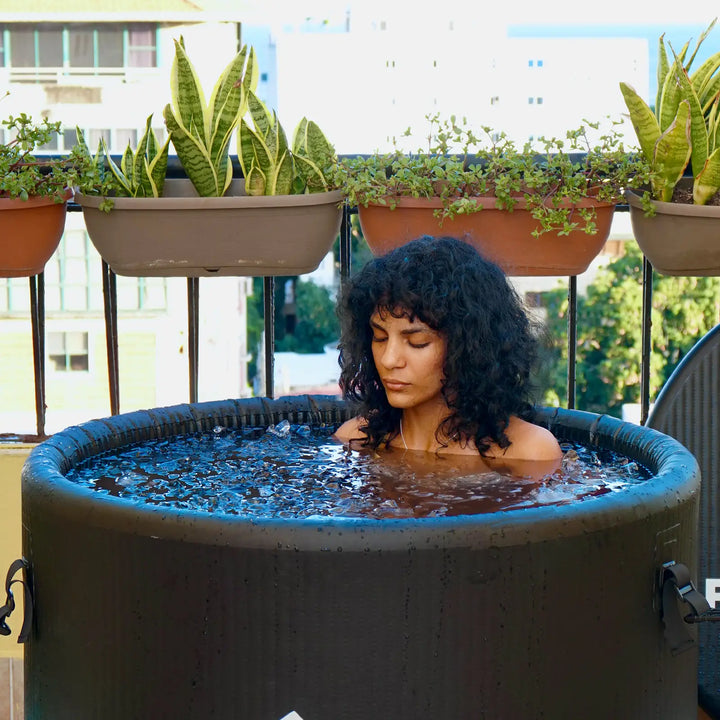 A curly-haired girl is sitting in an ice bath tub on a balcony, taking an ice bath.